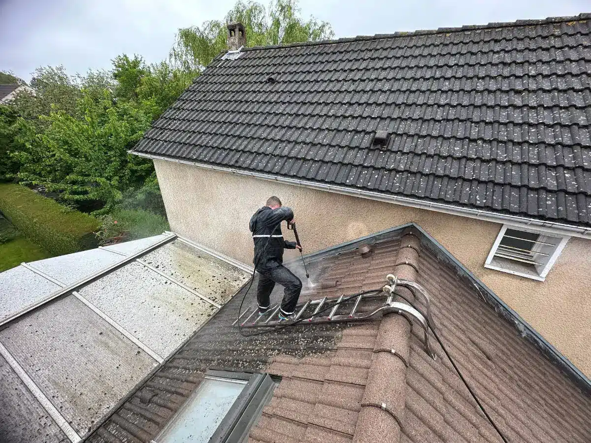 Francky Adnot, en train de mousser, une toiture au moyen d'un nettoyeur haute pression, il retire les salissures présentes sur une toiture en tuiles dans les Yvelines
