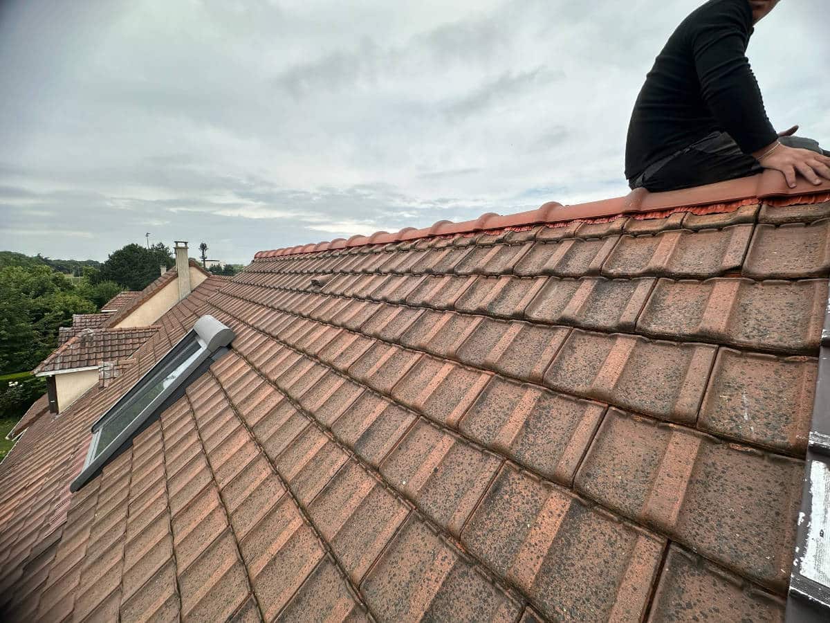 Gros plan sur une toiture en cours de réparation avec un artisan entre intervenir sur un faîtage abîmé, suite à des intempéries dans les Yvelines